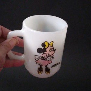 May include: White ceramic mug with a cartoon image of Minnie Mouse wearing a pink dress and yellow bow. The text "MINNIE" is printed below the image.