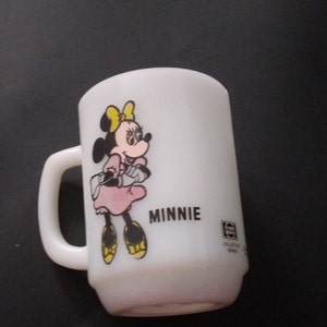 May include: White ceramic mug with a cartoon image of Minnie Mouse wearing a pink dress and yellow shoes. The mug has the word "MINNIE" printed on the front and a "Collector's Series" logo on the bottom.