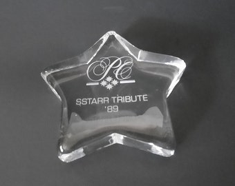 May include: A clear glass star-shaped paperweight with the inscription "SStarr Tribute '89" and a logo with the letters "PC" and three stars.