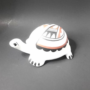May include: White ceramic turtle figurine with a painted geometric design in black, red, and orange on its shell.