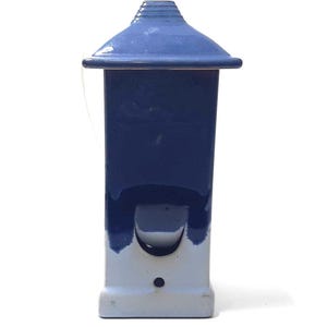 May include: A small, ceramic birdhouse in shades of blue. The roof is a darker blue, with a lighter blue body and base. The birdhouse has a small opening and a small hole at the bottom.