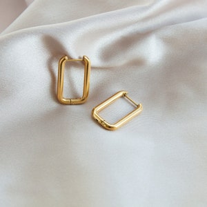 May include: A pair of gold-toned rectangular hoop earrings. The earrings are made of a thick metal and have a simple, modern design.