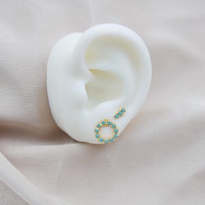 May include: A pair of gold earrings with turquoise stones. One earring is a small bar with three stones, and the other is a circle with a ring of stones.