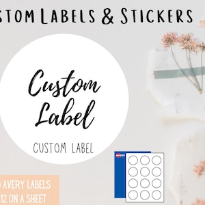 May include: A white circle with the text "Custom Label" in black cursive writing. The text "CUSTOM LABEL" is printed below the circle. The image also shows a sheet of 2" round Avery labels, product number 22817, with 12 labels on a sheet.