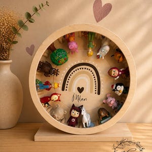 May include: A wooden display case with a circular frame, holding various small figurines. The case features a rainbow design with the name "Milan" and a heart. The figurines are of different colors and shapes, including animals and cartoon characters.
