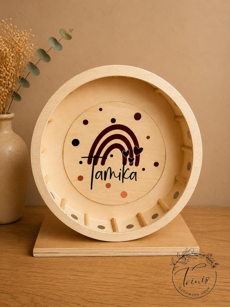 May include: A wooden hamster wheel with a personalized design. The wheel features a rainbow and heart design with the name "Tamika" in black script. The wheel is set on a wooden base and is a natural wood color.