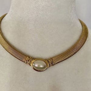 May include: A gold choker necklace with a large, oval-shaped faux pearl set in a gold frame with small clear rhinestones.