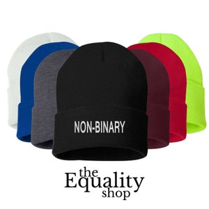 Puede incluir: Una colección de gorros en varios colores, incluyendo blanco, azul, gris, negro, burdeos, rojo y verde neón. El gorro negro tiene el texto "NON-BINARY" en blanco. El logotipo de The Equality Shop está en la parte inferior.