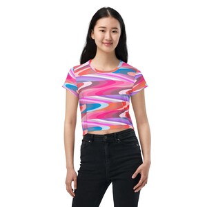 Könnte beinhalten: Ein bauchfreies T-Shirt mit einem abstrakten Druck in Pink, Blau und Orange. Das Shirt hat kurze Ärmel und einen runden Ausschnitt.