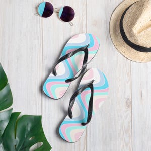 May include: A pair of blue, pink, and white flip flops with a wavy pattern. The flip flops have black straps.