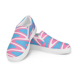 Pode incluir: Par de sapatos slip-on com sola branca. Os sapatos apresentam um padrão repetitivo de linhas onduladas em azul claro, rosa e branco. Os sapatos são projetados para uso casual.