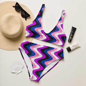 May include: A pink, blue, black and white striped swimsuit with a wavy pattern. The swimsuit has a halter top and high-waisted bottoms.