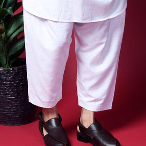 May include: A pair of brown leather sandals with a strap across the foot and an open toe. The sandals are worn by a person wearing white pants.