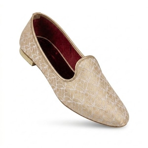 May include: A gold-colored loafer with a textured, patterned design. The shoe has a rounded toe and a low heel. The interior is lined with a deep red fabric. The shoe is designed for comfort and style.