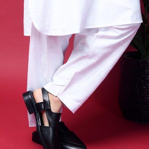 May include: A pair of black leather sandals with an open toe and ankle strap. The sandals have a pointed toe and a low heel.