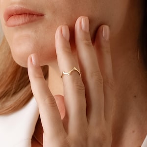 Könnte beinhalten: Ein goldener Ring mit einem gezackten, spitzen Design. Der Ring wird am Mittelfinger einer Hand getragen.