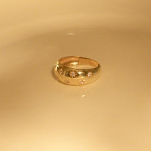 May include: A gold ring with a rounded band and small, clear stones set in a star shape.