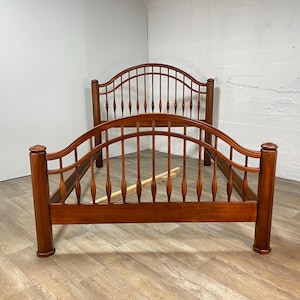 May include: A wooden bed frame with a warm, reddish-brown finish. The headboard and footboard feature a curved design with vertical spindles. The bed frame is made of solid wood and has a classic, traditional style.