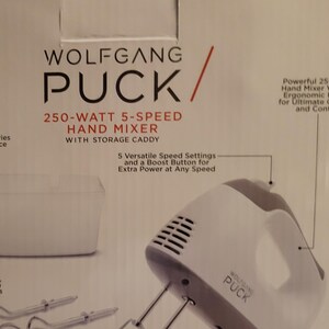 May include: A white Wolfgang Puck 250-watt 5-speed hand mixer with a storage caddy, dough hooks, and twisted wire beaters. The packaging displays the product name, power specifications, and features including an ergonomic handle and safety lock.