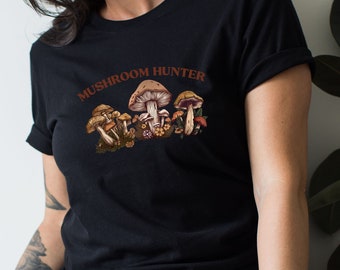 May include: Black t-shirt with the text "Mushroom Hunter" in brown letters. The shirt features a graphic of several mushrooms in various shades of brown and beige.