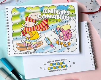 May include: A mini coloring book with paper dolls. The cover features a colorful illustration of two friends skiing in winter. The title of the book is "Amigos Canarios Paper Dolls".