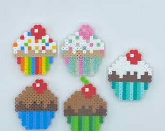May include: Five colorful cupcake designs made with perler beads. The cupcakes are decorated with sprinkles, frosting, and cherries.