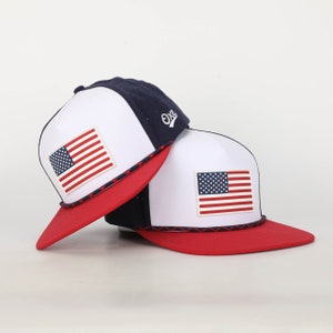 May include: Two white and blue baseball caps with red brims and an American flag patch on each. The caps have a navy blue mesh back and a white rope trim.