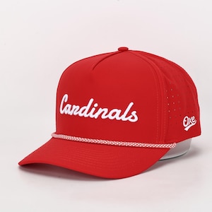 May include: Red baseball cap with the word "Cardinals" in white script across the front. The cap has a white rope detail along the brim and the word "Oke" in white on the side. The cap is made of a breathable material.