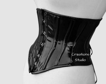 May include: A black patent leather corset with a busk closure and a lace-up back. The corset has a sleek, shiny finish and is designed to cinch the waist. The text "Creations Studio" is printed on the right side of the corset.