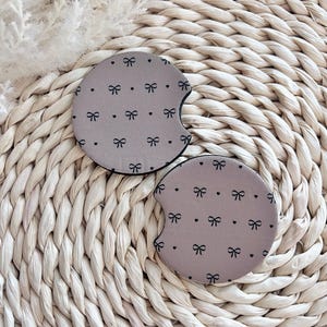 May include: Two brown car coasters with a black bow and white dot pattern.