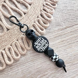 May include: Black and white anti social moms club keychain with a skull charm, black and white checkered bead, and black beads.