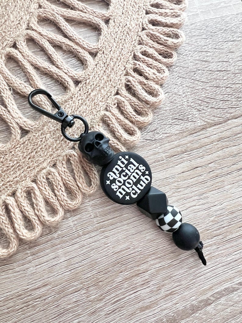 May include: Black and white anti social moms club keychain with a skull charm, black and white checkered bead, and black beads.