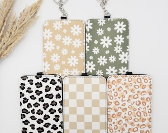 May include: Five rectangular keychains with different patterns: daisy, leopard, and checkered designs. The daisy keychains have a beige and green background with white flowers. The leopard print keychains have black and brown spots. The checkered keychain has a beige and white pattern.