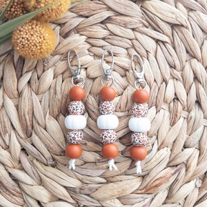 May include: Three brown and white beaded keychains with a leopard print design. Each keychain has a silver metal ring and a silver metal clasp.