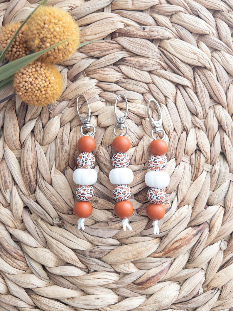 May include: Three brown and white beaded keychains with a leopard print design. Each keychain has a silver metal ring and a silver metal clasp.