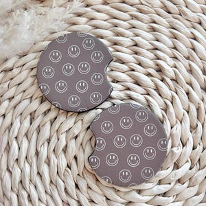 May include: Two brown round drink coasters with a white smiley face pattern.
