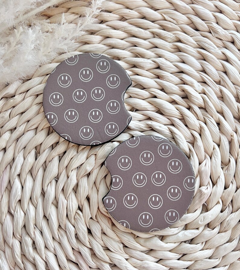 May include: Two brown round drink coasters with a white smiley face pattern.
