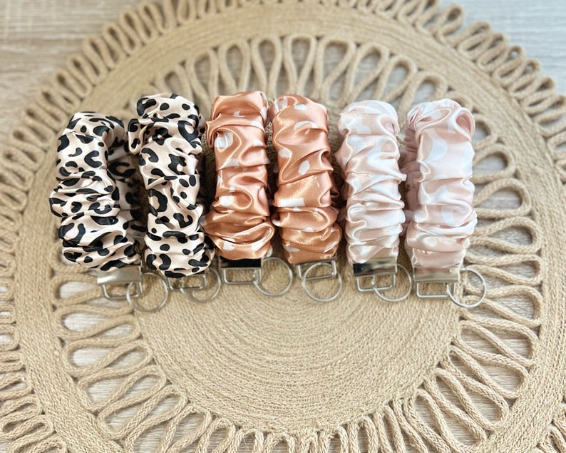May include: Seven keychains with different patterned fabric covers. The keychains are in a variety of colors, including brown, pink, and white. The fabric covers are all made of a soft, silky material.