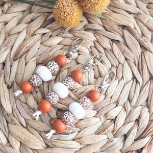 May include: Three brown and white leopard print silicone beaded keychains with silver key rings. The keychains are on a woven brown background.