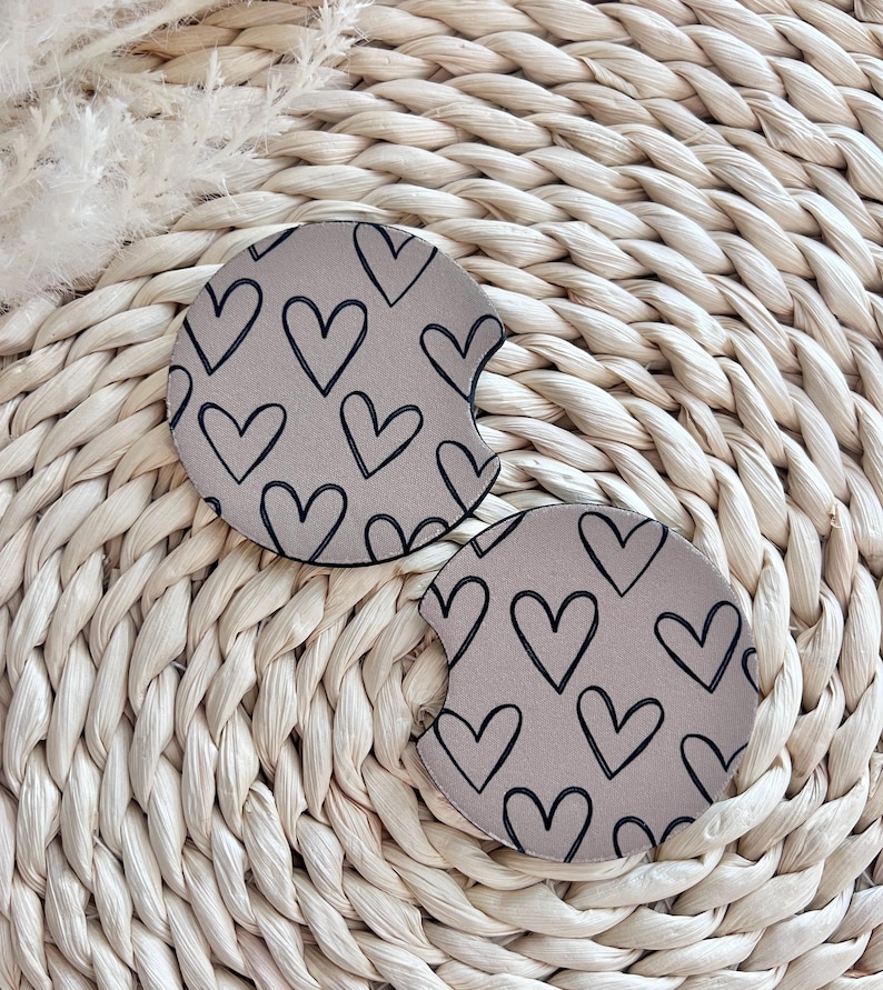 May include: Two beige car coasters with a black outline of hearts pattern.
