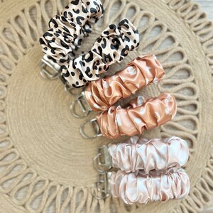 May include: Five keychains with different patterns. The keychains are made of soft, silky fabric and have a silver metal ring. The patterns include leopard print, peach with white dots, and pink with white dots.
