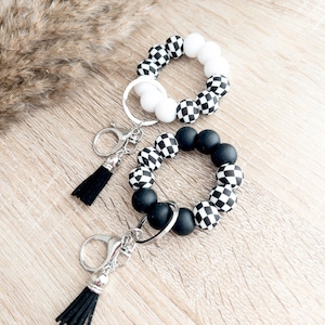 May include: Three black and white checkered silicone beaded keychains with silver key rings and black tassels.