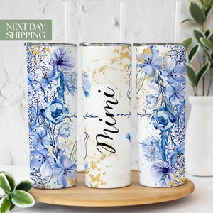 May include: Three stainless steel tumblers with a white background and blue floral design. The middle tumbler has the word "Mimi" written in black cursive.
