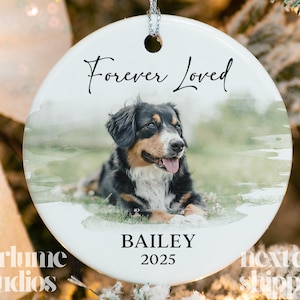 May include: A white ceramic ornament with a photo of a dog, featuring the text "Forever Loved" in script. The dog is black, brown, and white, with the name "BAILEY" and the year "2025" below the photo. The ornament has a silver hanging loop.
