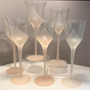 Puede incluir: Un juego de seis copas de vino de cristal esmerilado. Cada copa tiene un tallo largo y un cuenco ancho en forma de tulipán con un diseño geométrico. La base y el tallo son de color rosa suave, mientras que el cuenco es transparente.