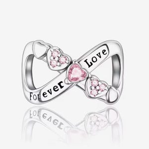 May include: Silver charm with an infinity symbol design. The charm features three heart-shaped accents with pink gemstones and the words "Forever Love". The charm is reflective.