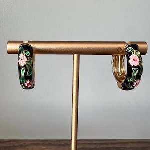 May include: A pair of gold hoop earrings with black enamel and pink and green floral designs.