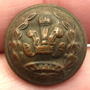 May include: A round, antique bronze button with a detailed embossed design. The button features a crown at the center, surrounded by laurel leaves, and the word "BOWEN" is inscribed at the bottom. The button has a slightly aged appearance.