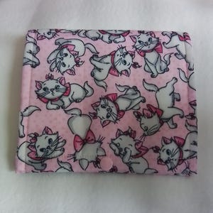 May include: A pink fabric case featuring a repeating pattern of white cartoon cats with pink bows. The cats are in various poses against a background of small white dots. The case has a pink button closure.