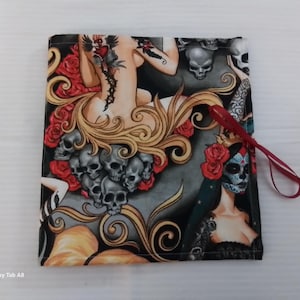 May include: Square fabric item with a tattoo-style design featuring skulls, roses, and a woman with long blonde hair. The artwork includes a Day of the Dead sugar skull and a red ribbon attached to the item.
